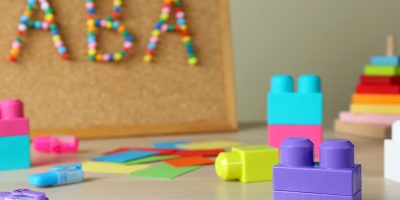Cork board with abbreviation ABA (Applied behavior analysis) at table, focus on colorful blocks